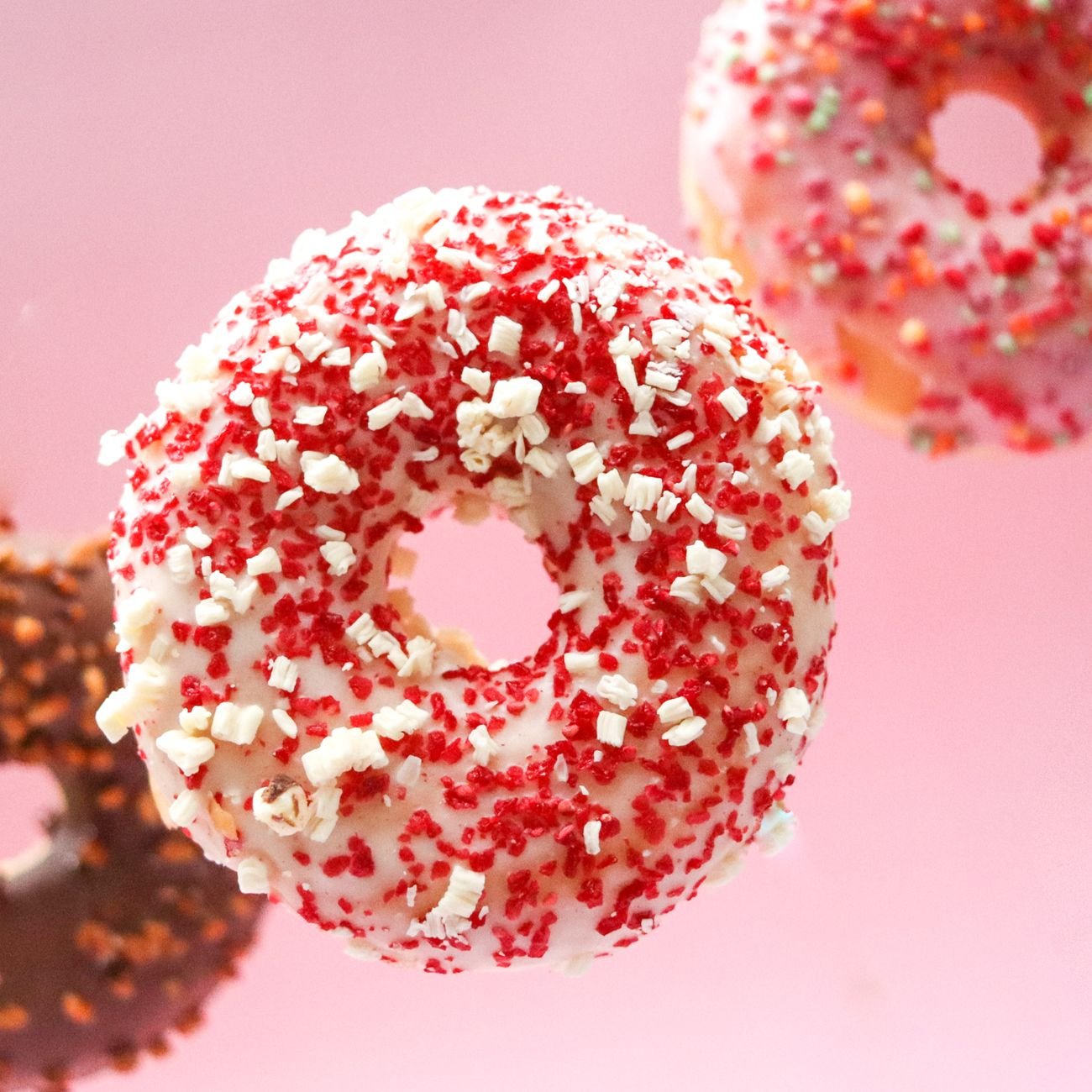 Vibrant donuts with colorful sprinkles on a soft pink background.